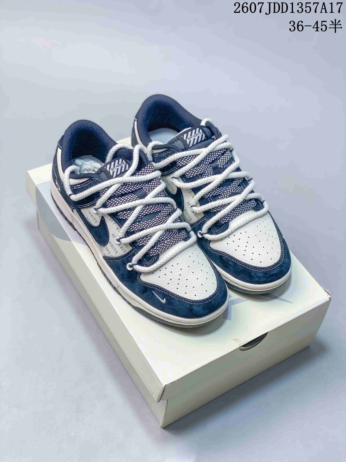 Pair of navy and white Nike SB Dunk Low sneakers displayed on a shoebox, showing layered rope laces and contrasting panels.