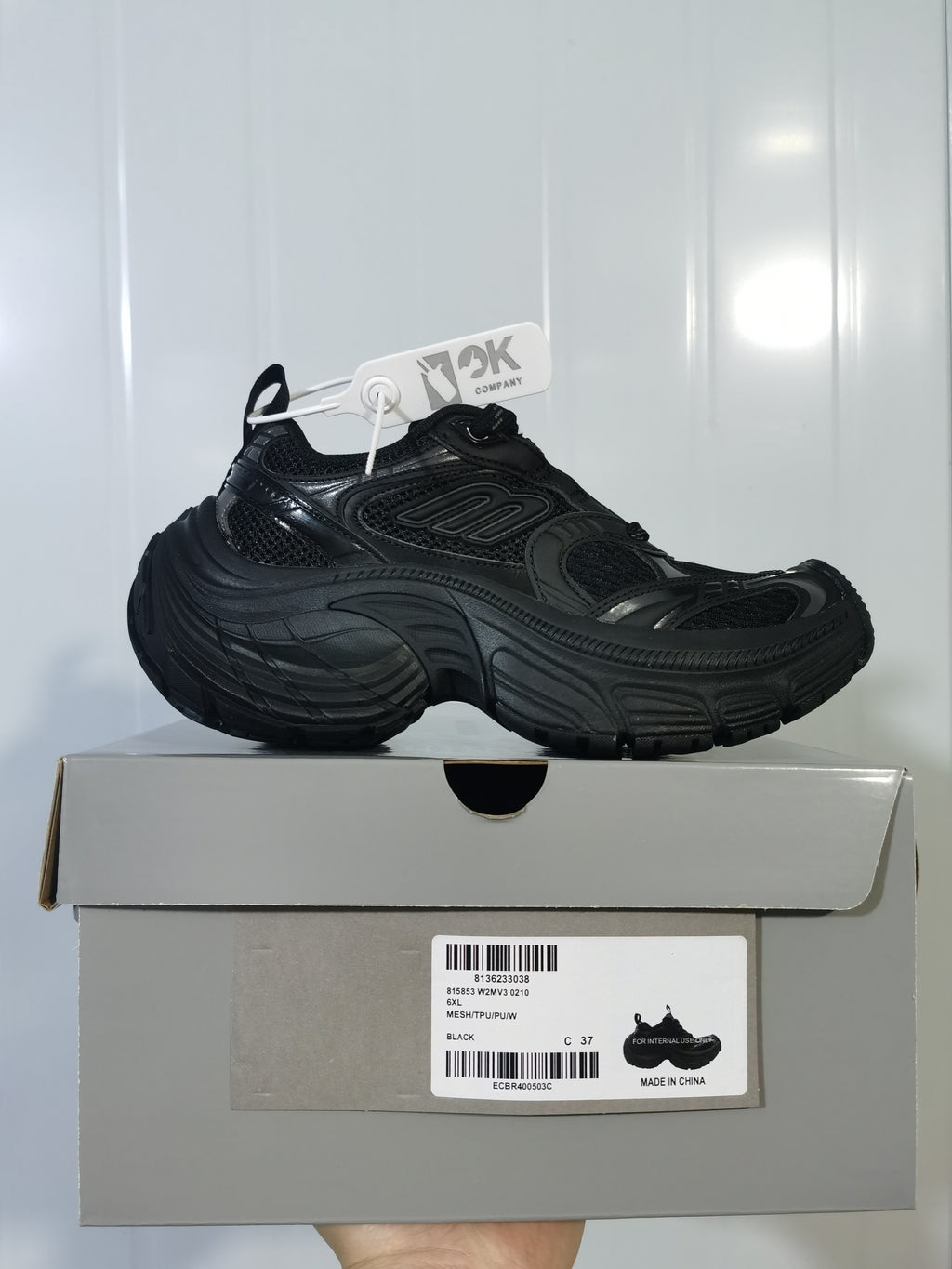 Black chunky mesh sneaker displayed on a shoe box, with a visible box label and attached tag.