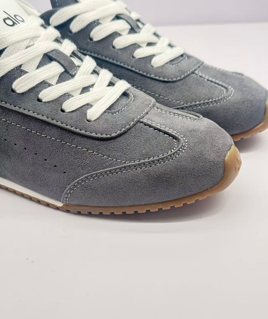 Close-up of the stitched toe panel, gray upper, white laces, and brown outsole edge.