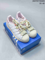 Pair of white Adidas Superstar sneakers with pastel decorative laces displayed on a blue Adidas shoe box.