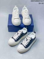 White and navy Dior low-top sneakers arranged around a blue Dior shoe box, showing both colorways and their lace-up construction.