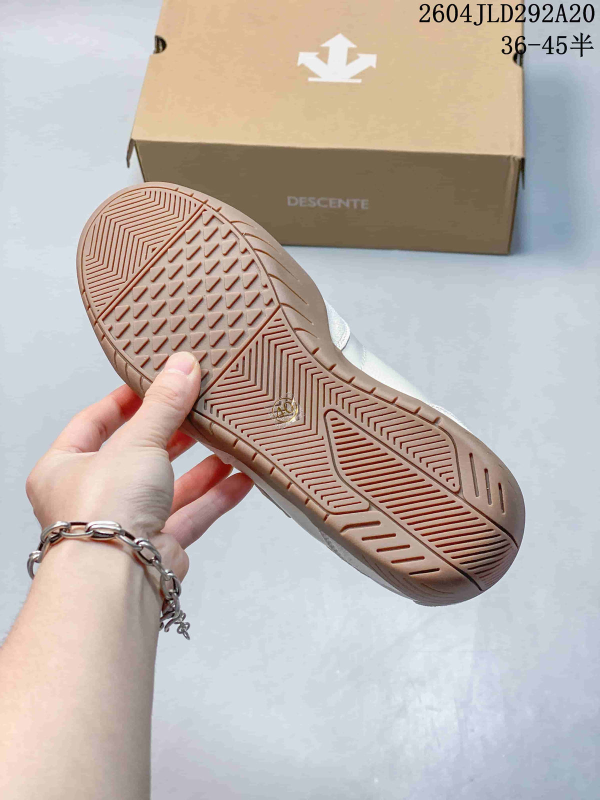 Close-up of the patterned gum-colored outsole on a cream Descente sneaker.