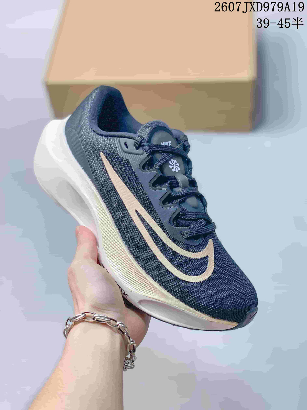 Dark navy Nike Zoom Fly 5 PRM sneaker with a light-colored side logo and white sculpted sole, held in front of a shoe box.