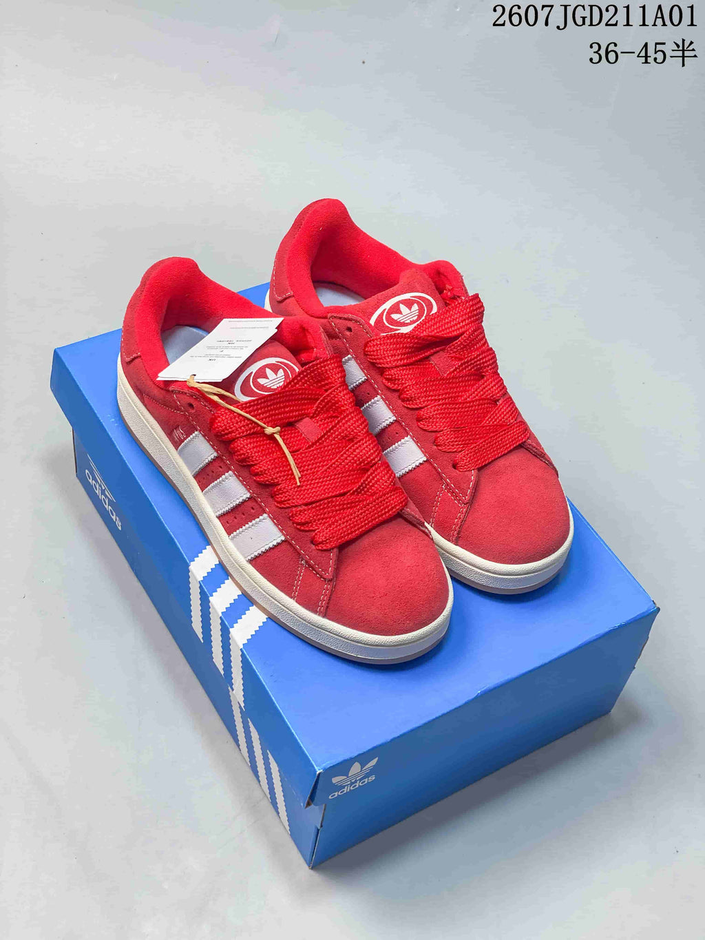 Red Adidas Campus sneakers with white side stripes shown on a blue shoe box