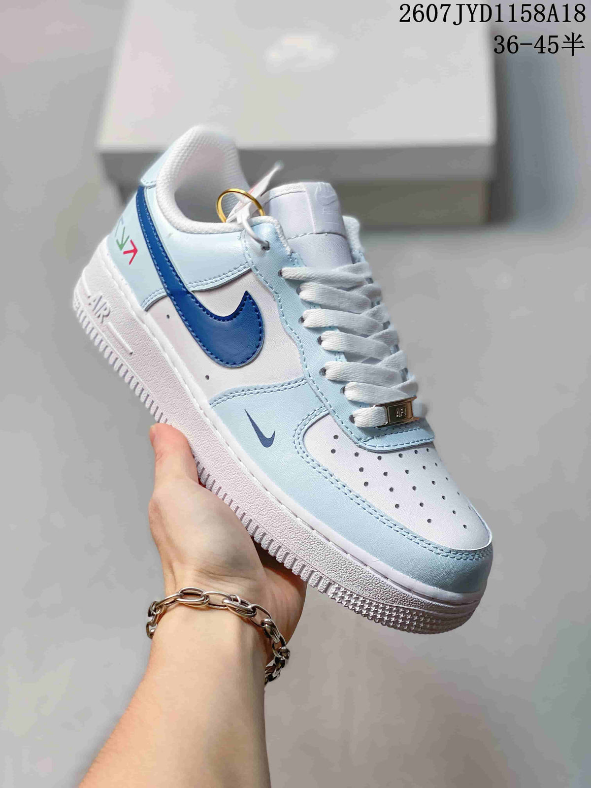 Angled side view of the white and light blue low-top sneaker showing the dark blue Swoosh, white midsole, blue heel detailing, and lace accessory.