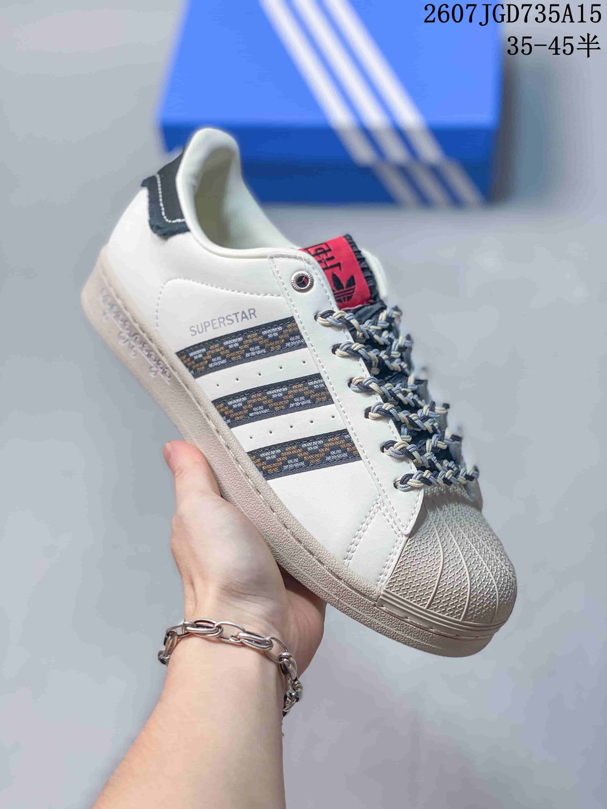 Angled side view of the sneaker showing the SUPERSTAR side text, patterned stripes, shell toe, and black heel tab.