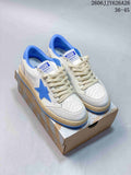 Pair of white and blue low-top sneakers with blue star details, cream laces, and a distressed beige-toned midsole displayed on a shoe box.