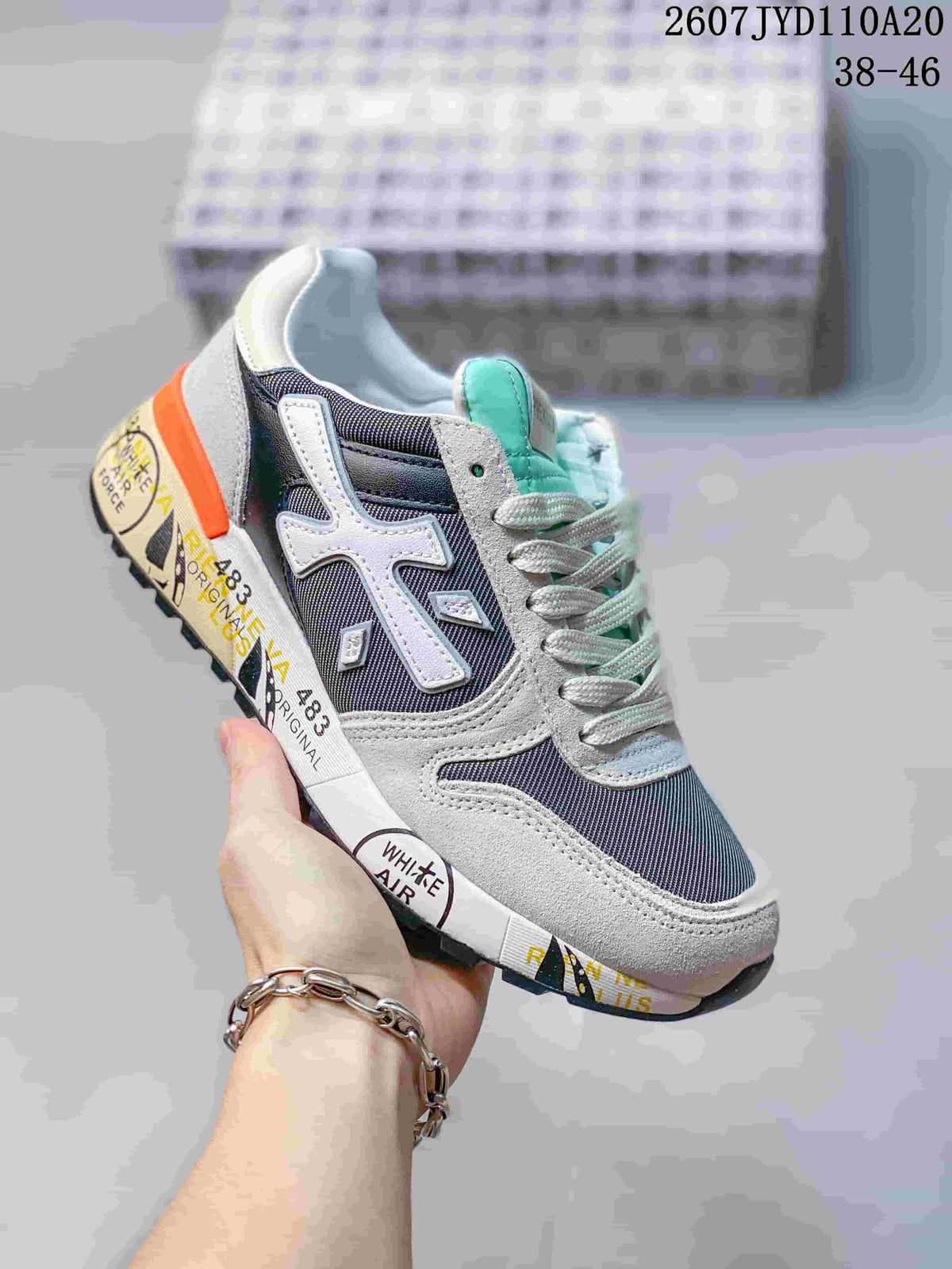 Angled side view of a grey and navy Premiata sneaker with mint-green tongue accents, orange heel detail and a black outsole; image text shows 2607 TYD110A20 and 38–46.