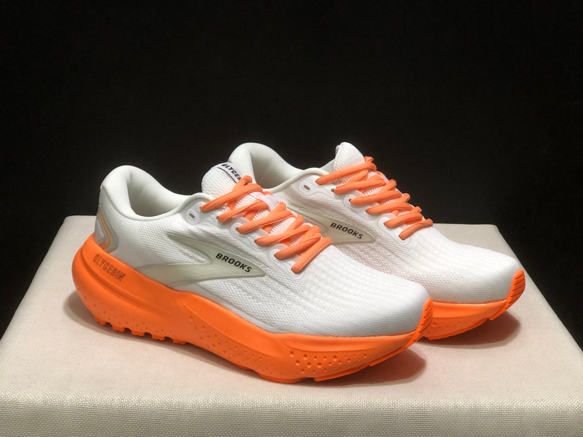 Front three-quarter view of the paired Brooks sneakers with orange laces and thick orange soles.