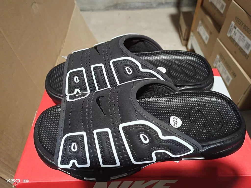 Black Nike Air-style slide sandals with perforated upper, layered side panels, textured footbed, and black outsole.