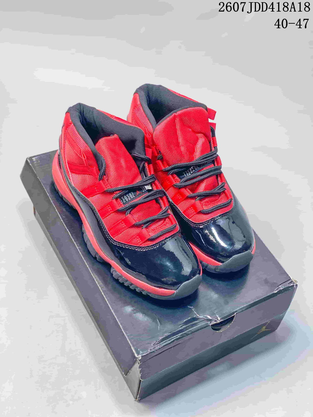 Black and red high-top sneakers with glossy black toe panels and red upper sections displayed on a dark shoebox.