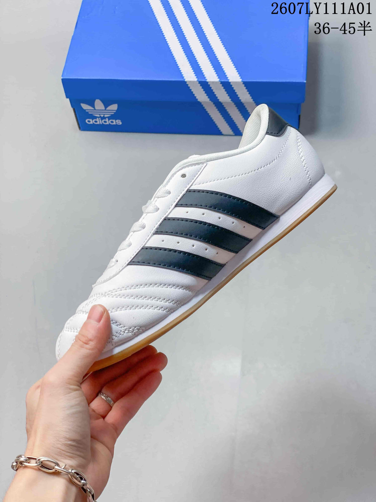 Side profile of the white low-top shoe with dark stripes and a gum-colored outsole.