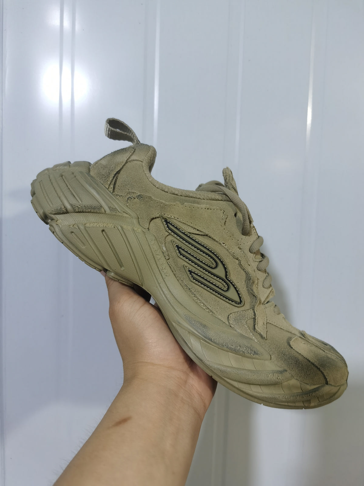 Angled view of the beige sneaker showing the lace-up upper, padded collar, heel pull tab, side detail, and sculpted sole.