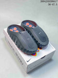 Nike Mind 001 slides in dark gray-black on a Nike Mind box, with the closed toe, perforated upper, and orange footbed details visible.