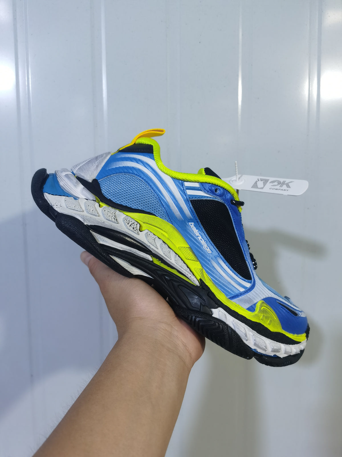 Side view of blue, white, black and yellow Balenciaga Triple S 2 sneakers held against a light background.
