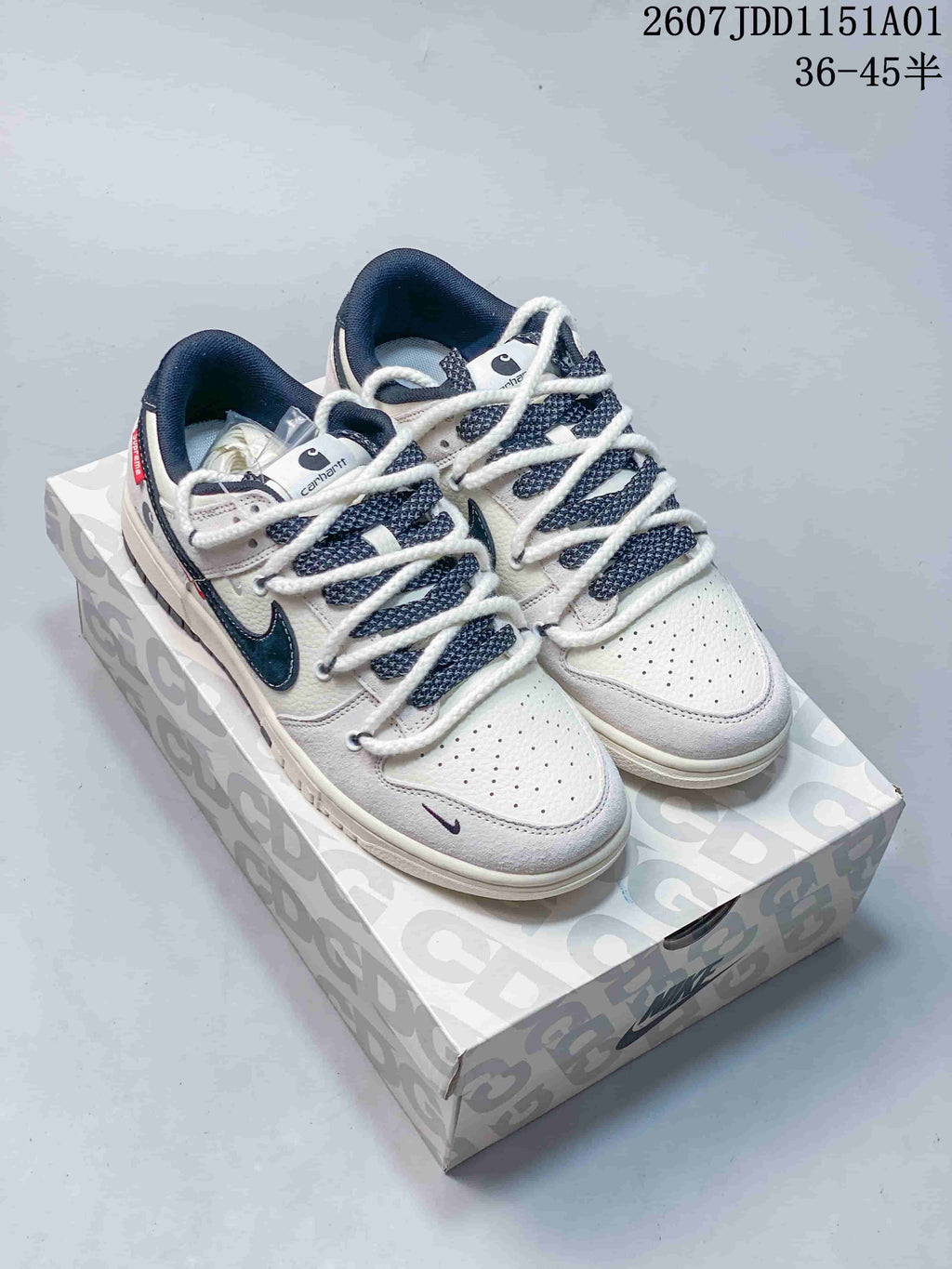 Pair of white and gray low-top sneakers with dark swooshes, patterned laces, and Carhartt branding details.