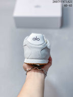 Rear view of the white sneaker showing the padded heel, Alo branding, white midsole, and gum outsole edge.
