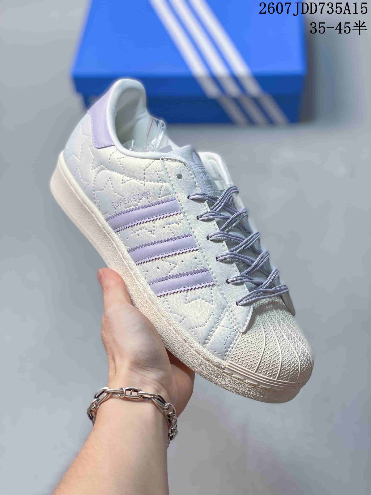 Angled side view showing Superstar branding, lavender three stripes, shell toe, and rubber cupsole.