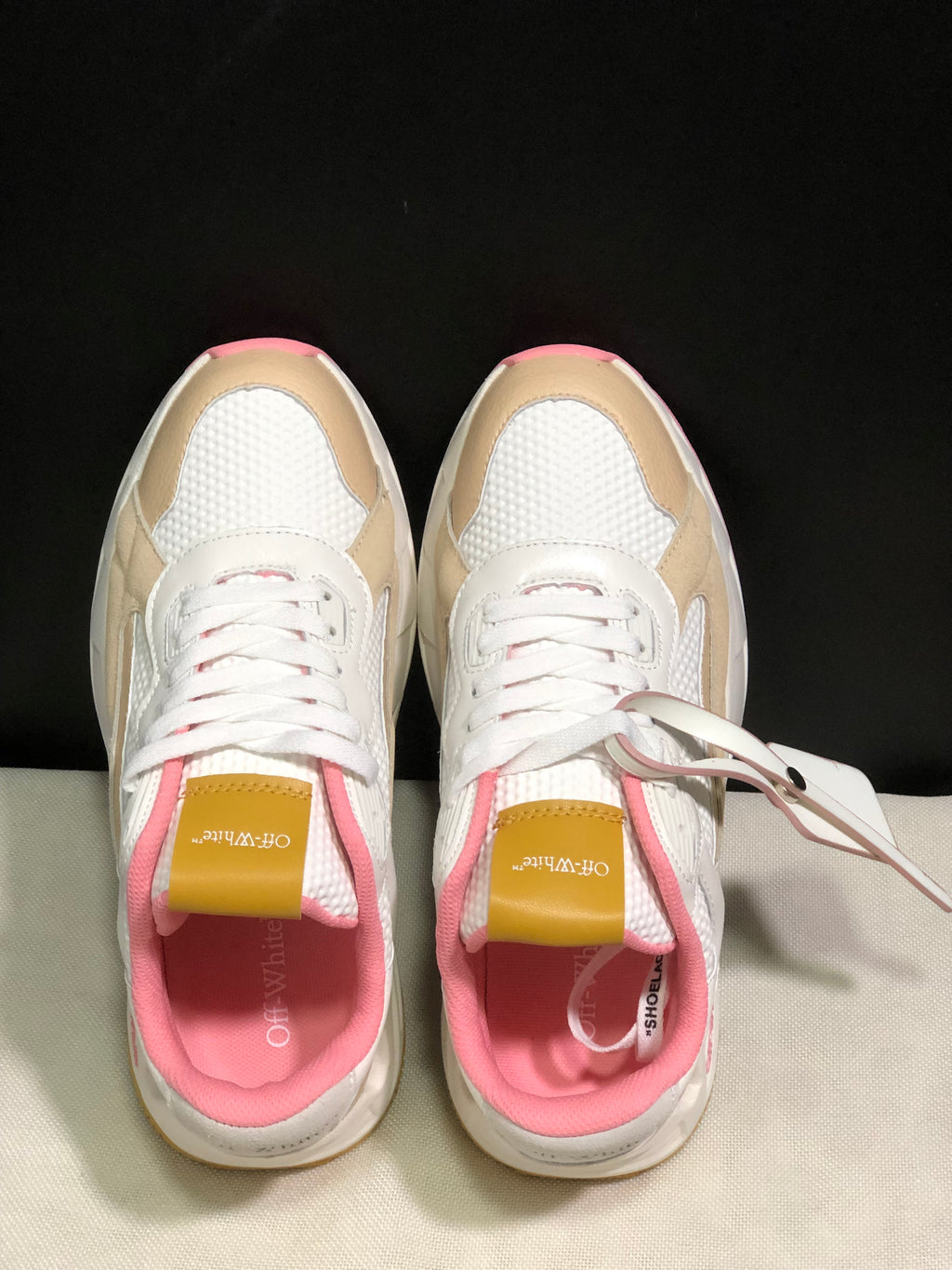 Top-down view showing the lace-up construction, textured white panels, beige overlays, pink lining and branded tongues.