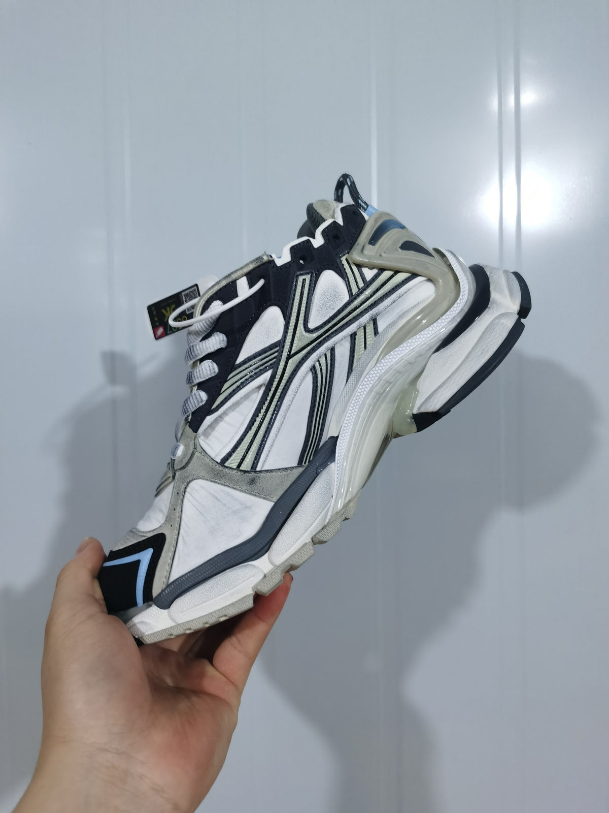 Side view of the white, black, gray, and cream Runner sneaker showing its layered panels and textured sole.