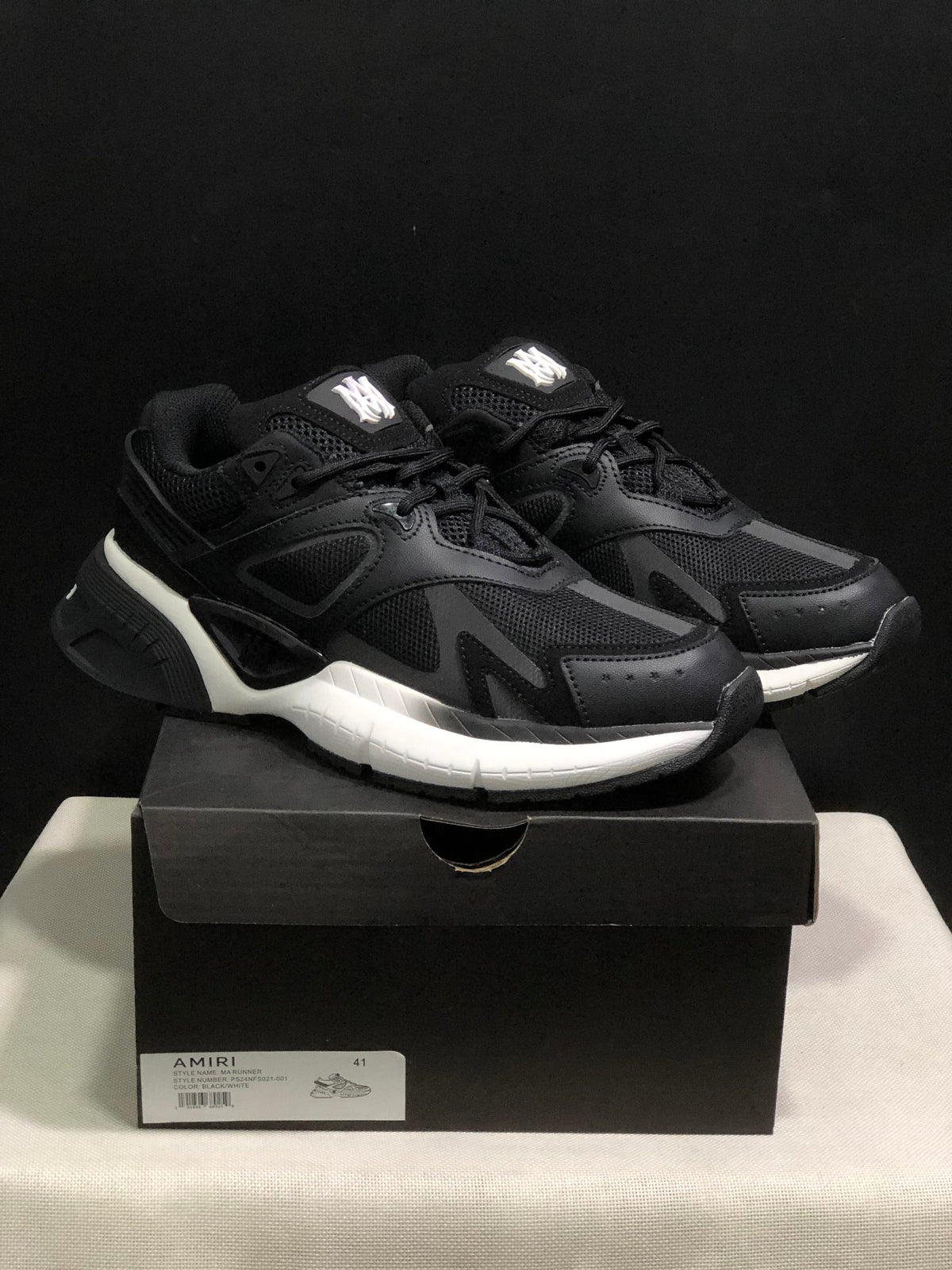 Three-quarter front view of the black and white AMIRI MA Runner sneakers on their shoebox, with a visible size 41 box label.