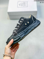 Side view of the black low-top sneaker showing metal eyelets, white stitching and the sculpted distressed-look sole.