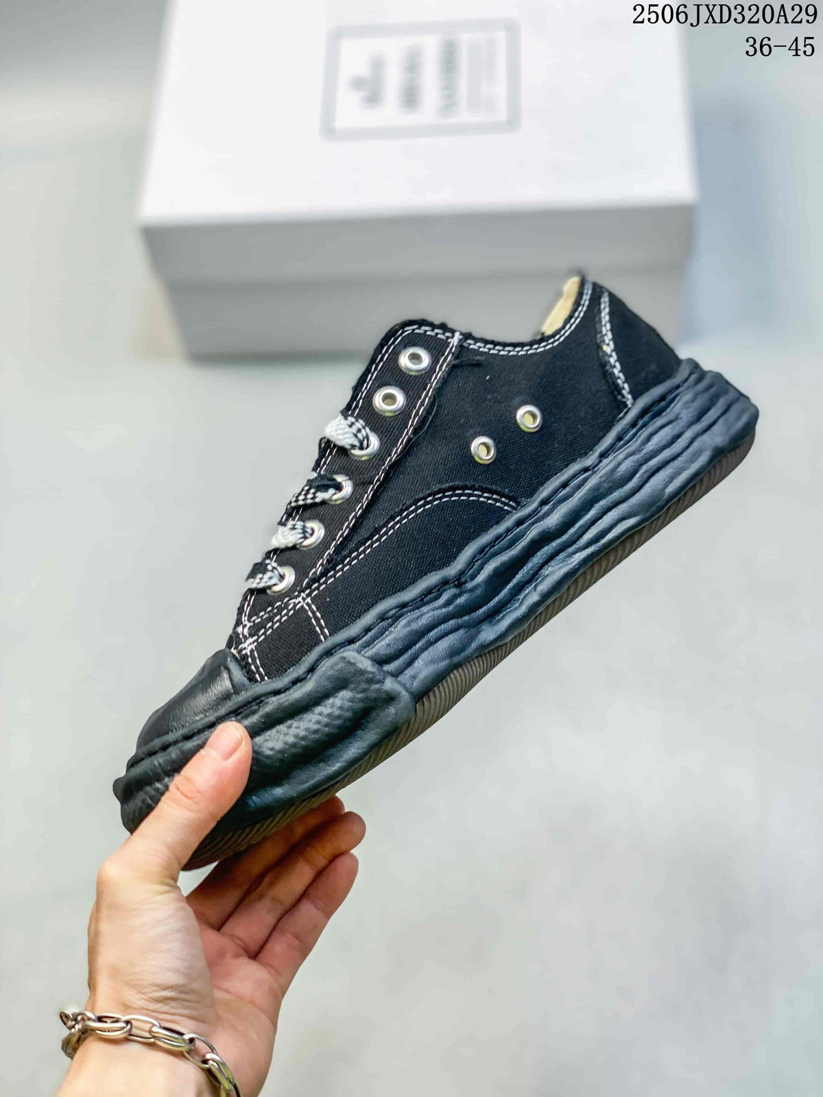 Side view of the black low-top sneaker showing metal eyelets, white stitching and the sculpted distressed-look sole.