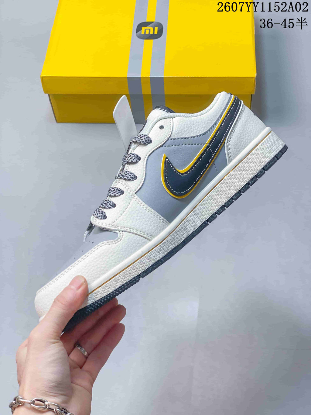 Side profile of the grey and white low-top sneaker with a dark, yellow-trimmed side detail