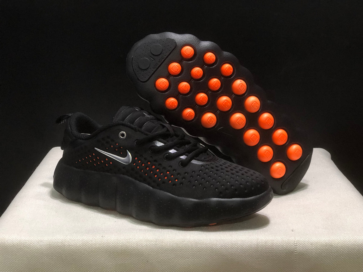 Angled view showing one sneaker's black upper and the outsole with raised orange circular elements.