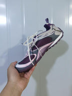 Top and angled view of the Skechers 5159 sneaker showing the layered upper, mesh sections, cream laces, and purple outsole.