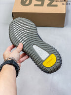 Underside view of the sneaker showing the ribbed gray outsole, textured tread, yellow Boost detail, and shoe box in the background.