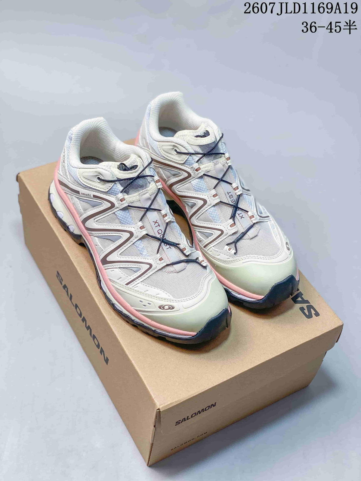 Pair of white Salomon XT-Quest sneakers with pink trim shown on a Salomon shoebox; overlay shows style code 2607JLD1169A19 and size range 36–45.5.