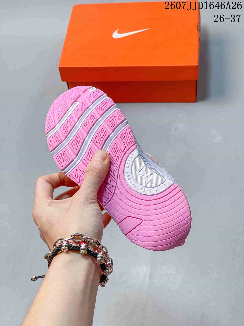 Pink patterned outsole of the children's training shoe held above an orange shoebox.