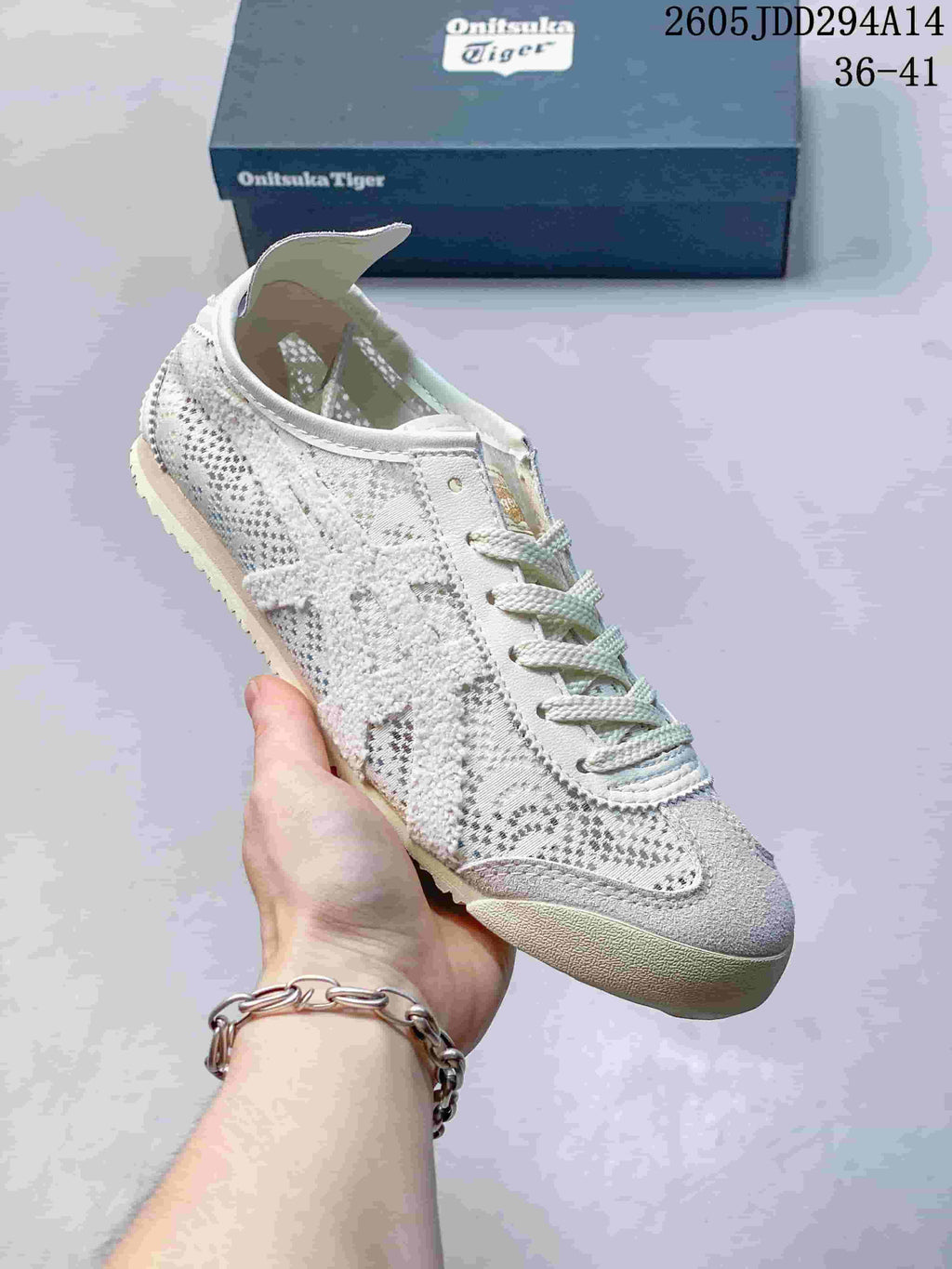 Close-up view of a light-colored Onitsuka Tiger sneaker showing the textured upper, stitched side panels, laces, and flat rubber outsole.