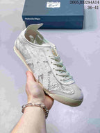 Close-up view of a light-colored Onitsuka Tiger sneaker showing the textured upper, stitched side panels, laces, and flat rubber outsole.
