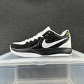 Side view of a black and white Nike low-top basketball shoe with a large white Swoosh and a small yellow heel accent.