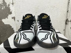 Front view of white and black sneakers with black laces and gold tongue embroidery