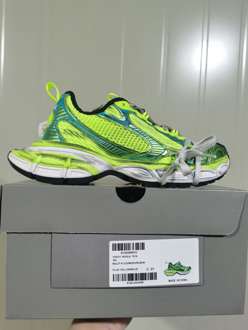 Side profile of the fluorescent yellow and blue sneaker displayed on its box, with the product label visible below.