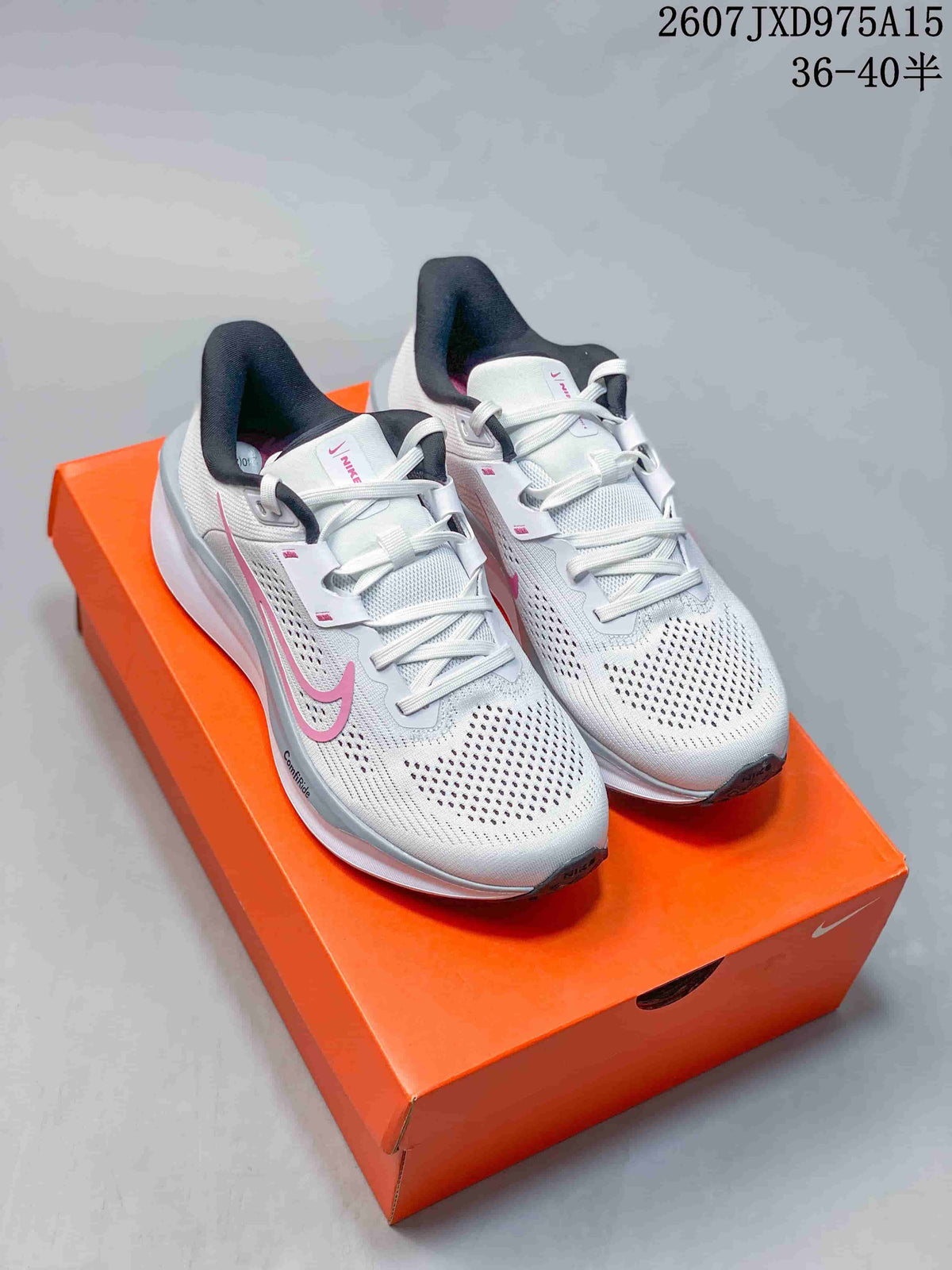 Pair of white and pink Nike Quest 6 running shoes displayed on an orange shoebox.