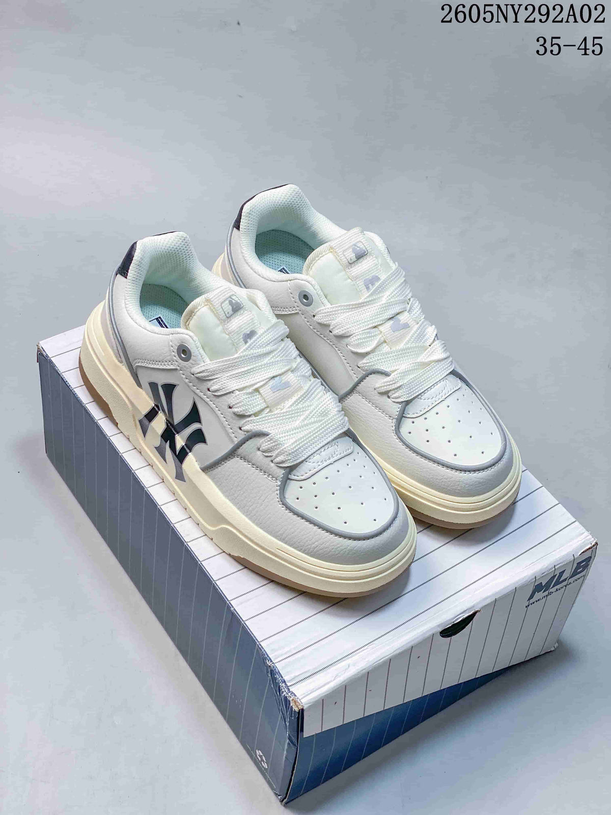 Pair of white MLB low-top sneakers with chunky cream-toned soles displayed on a shoe box; image text shows code 2605NY292A02 and EU size range 35–45.