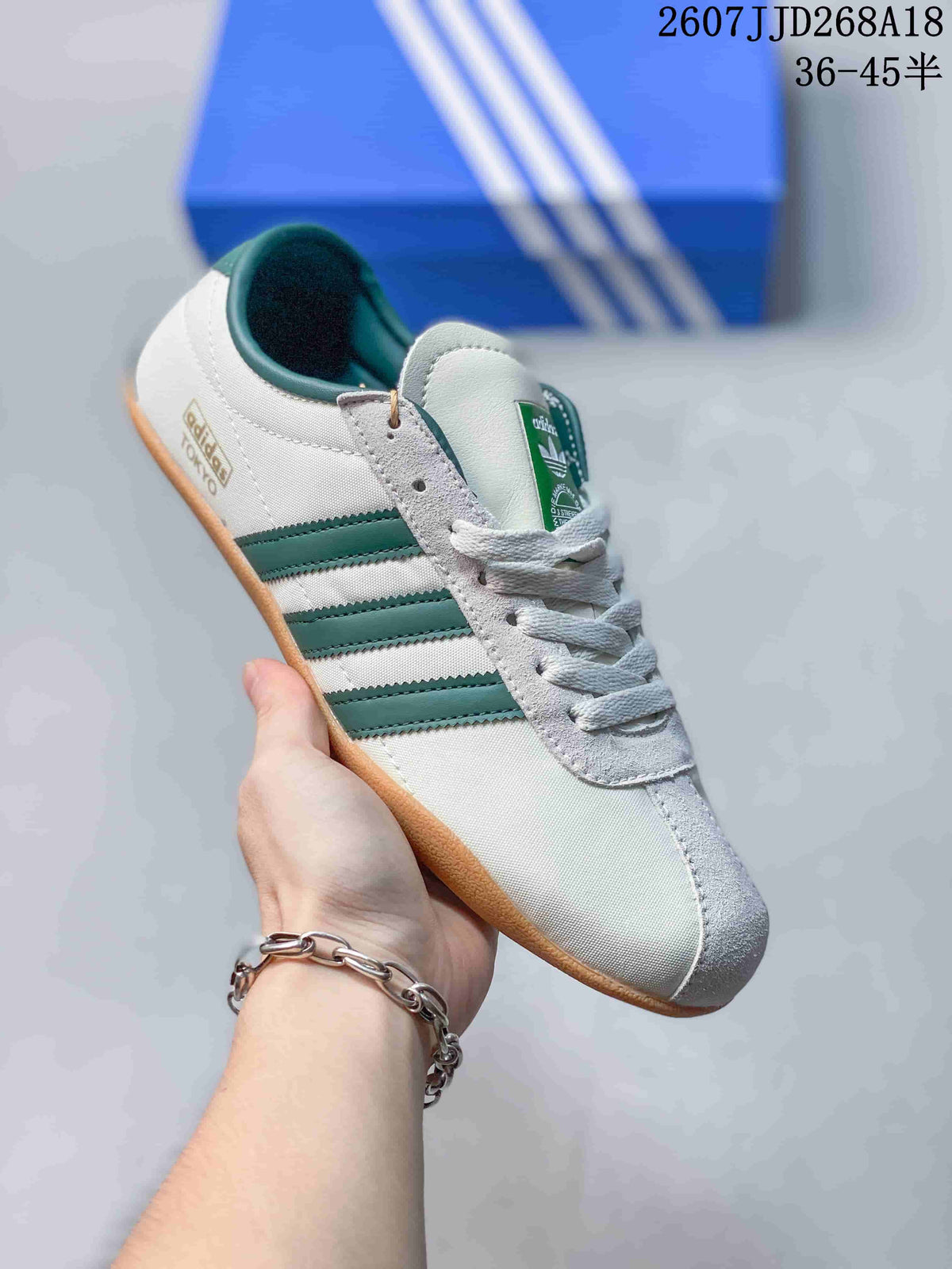 Close view of a white adidas Originals Tokyo sneaker with green three-stripe branding, white laces, trefoil tongue label, and gum-colored outsole.