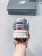 Rear view of a gray and white New Balance 509 sneaker with red detailing, padded collar, and layered heel construction.