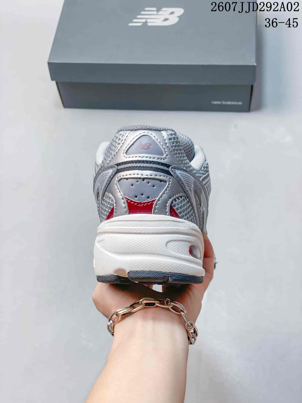 Rear view of a gray and white New Balance 509 sneaker with red detailing, padded collar, and layered heel construction.