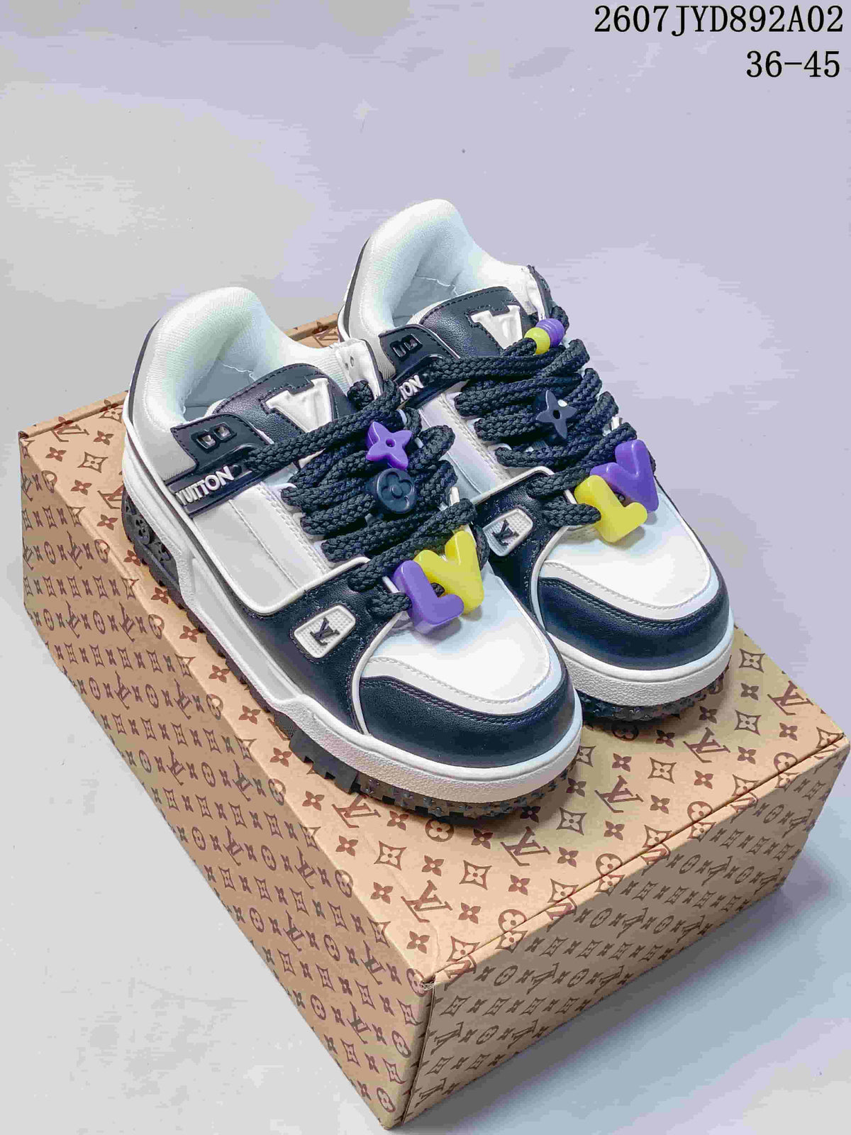 Pair of white and navy low-top sneakers with purple and yellow lace accents on a patterned box