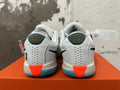 Rear view of white Nike basketball shoes with green heel tabs, orange heel accents, and blue outsoles