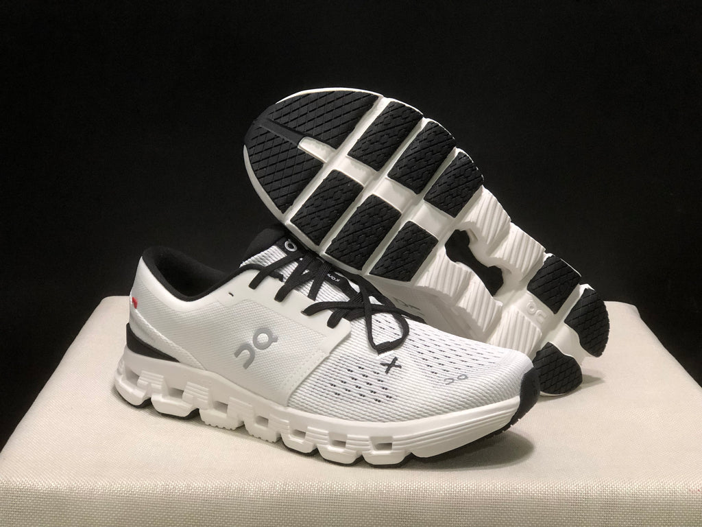 On Cloud X4 sneaker shown with its segmented outsole and black rubber traction sections facing upward.