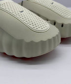 Close-up of the perforated beige upper and scalloped edge of the sandal sole.