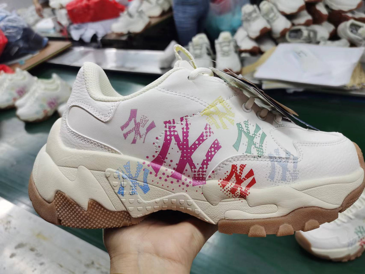 White MLB sneakers with multicolored painted-style lettering and logos, layered sole, and gum-colored outsole sections.