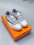 Pair of white and gray Jordan 1 low-top sneakers with monogram-style panels displayed on an orange shoebox.