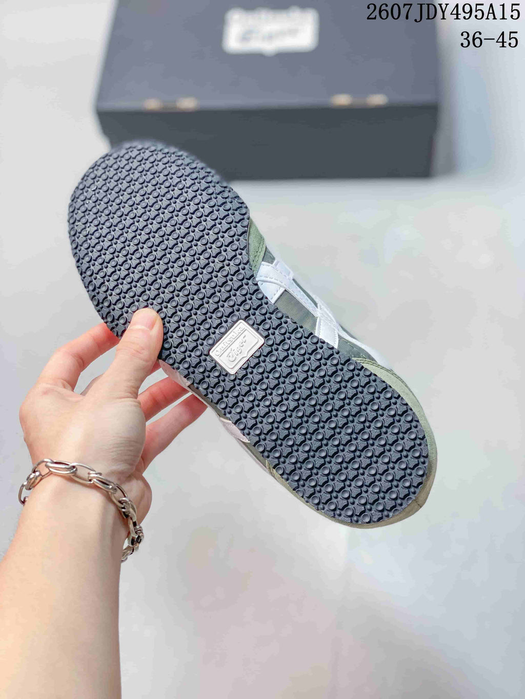 Underside of an Onitsuka Tiger Serrano sneaker showing the dark textured outsole and branding detail; style code and EU size range appear in the background.